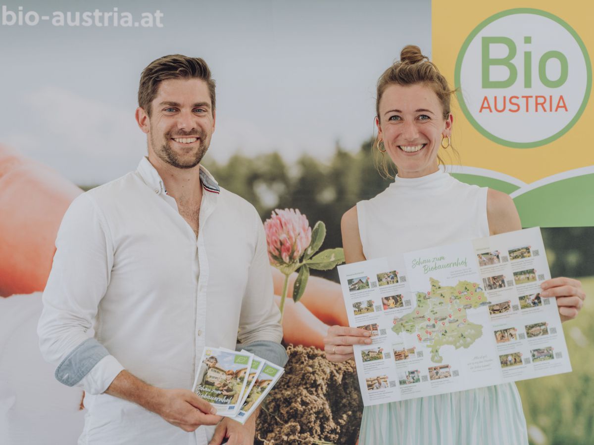 Mann und Frau halten Folder in den Händen, dahinter ein Poster von Bio Austria.