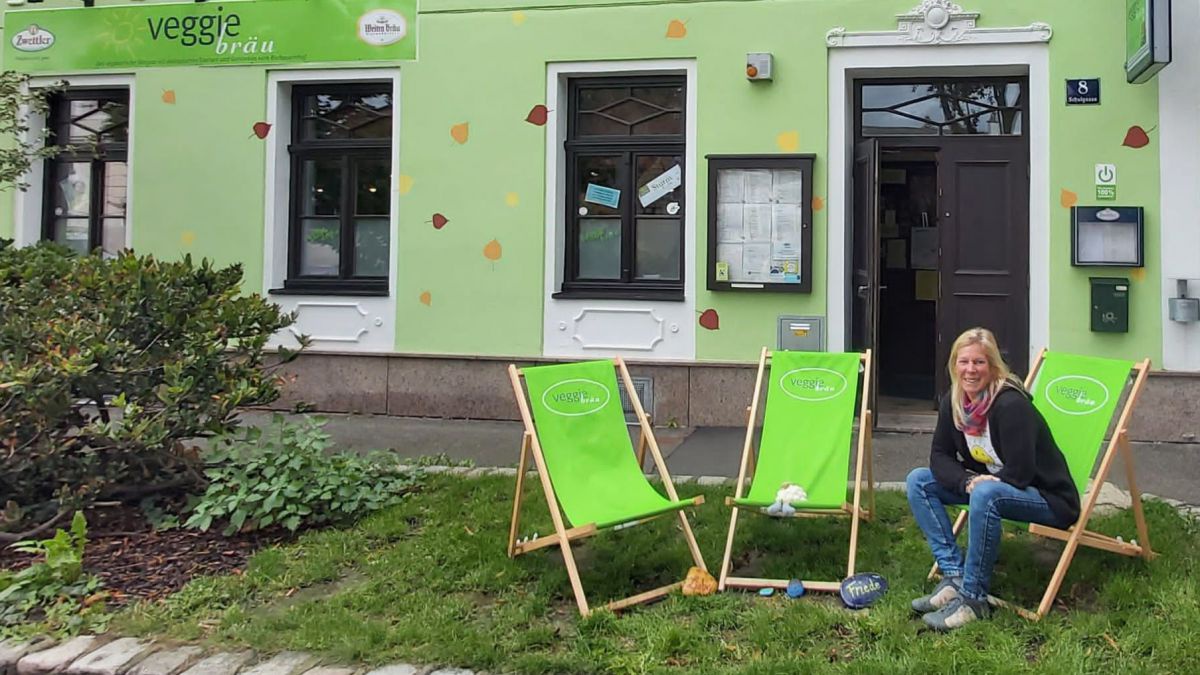 Grünes Haus, davor ein Rasenstreifen mit drei Liegesessel, in einem sitzt Christa Böhm.