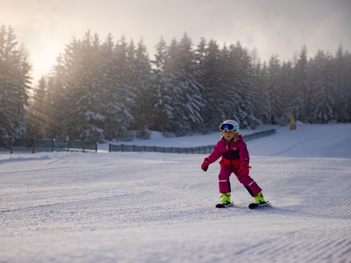 Kind fährt mit Skiern den Hang runter.