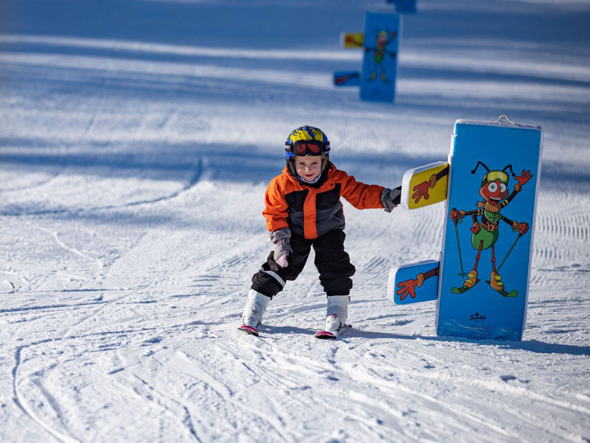 Kind fährt mit den Ski einen Parcours und muss dabei einer Figur die Hand geben.