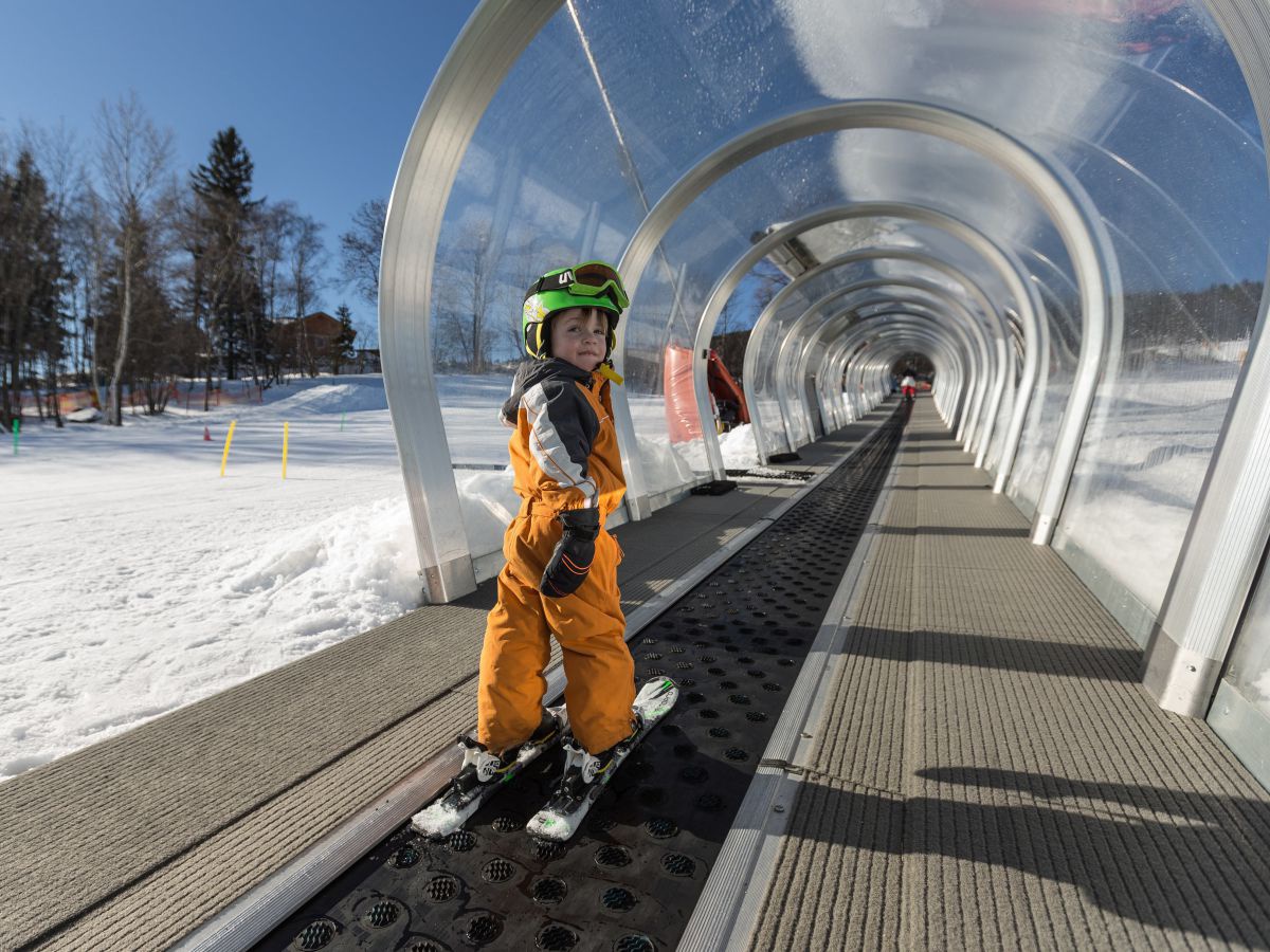 Kind mit Ski auf Förderband-Lift.