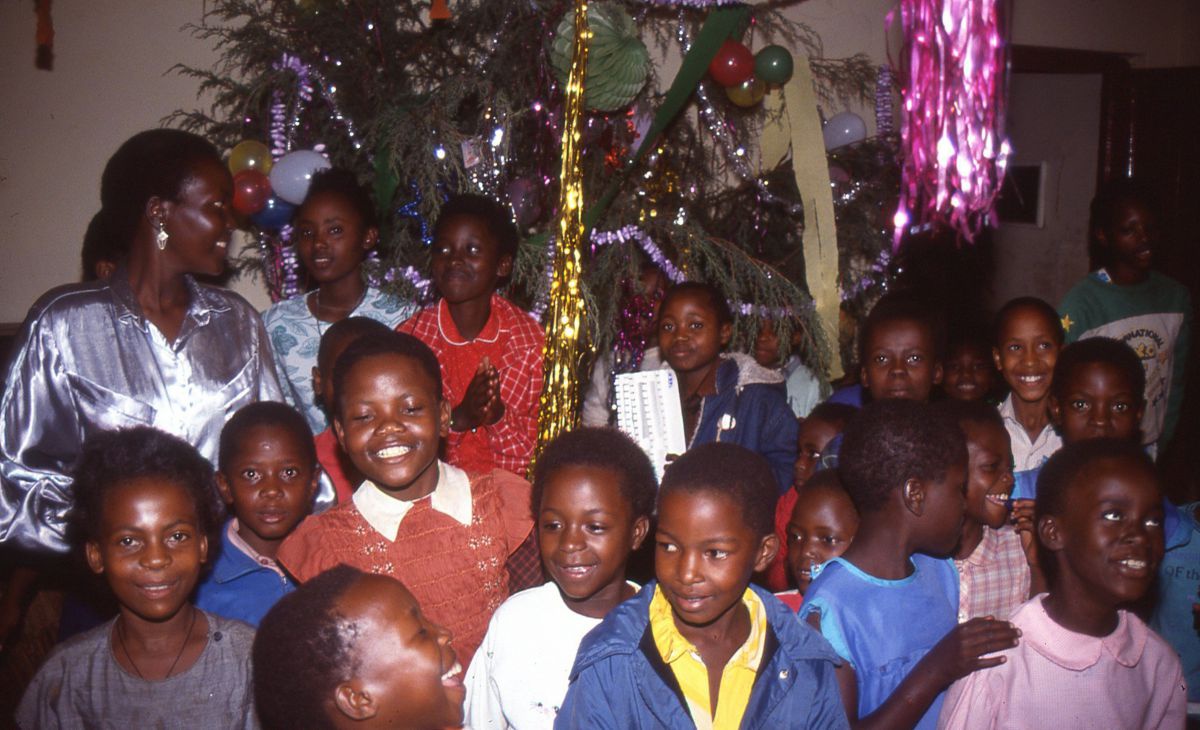 Gruppe von Waisenkindern, dahinter ein geschmückter Baum.