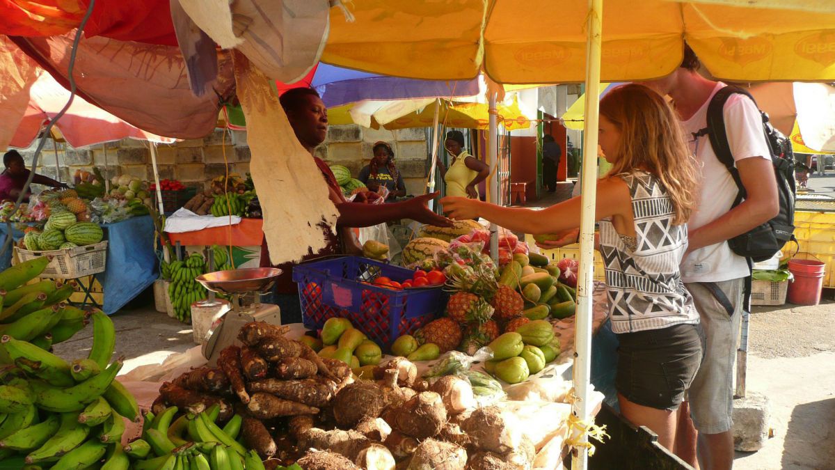 Eine weiße Frau und ein weißer Mann kaufen Obst auf einem afrikanischen Markt.