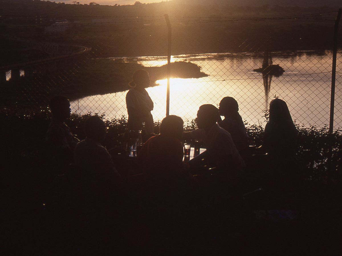 Sonnenuntergang. Gruppe von Leuten sitzt an einem Tisch oberhalb der Nilmündung.