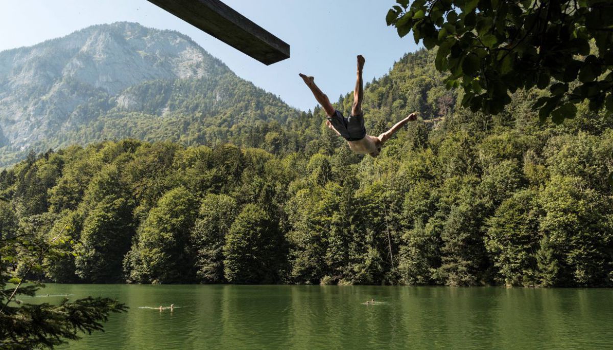 Mann springt von einem Sprungbrett aus ziemlicher Höhe in den See. 