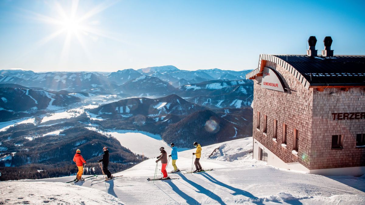 Eine Gruppe von Sschifahrer*innen beim Terzerhaus an Gipfel der Gemeindealpe mit Blick ins Tal auf den zugefrorenen Erlaufsee.