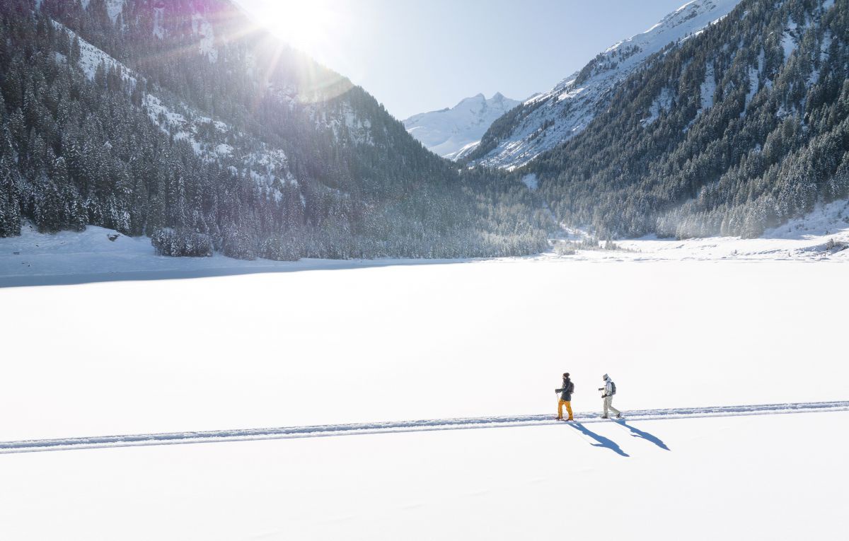 2 Schneeschuhwanderer gehen durch eine tief verschneite Landschaft.