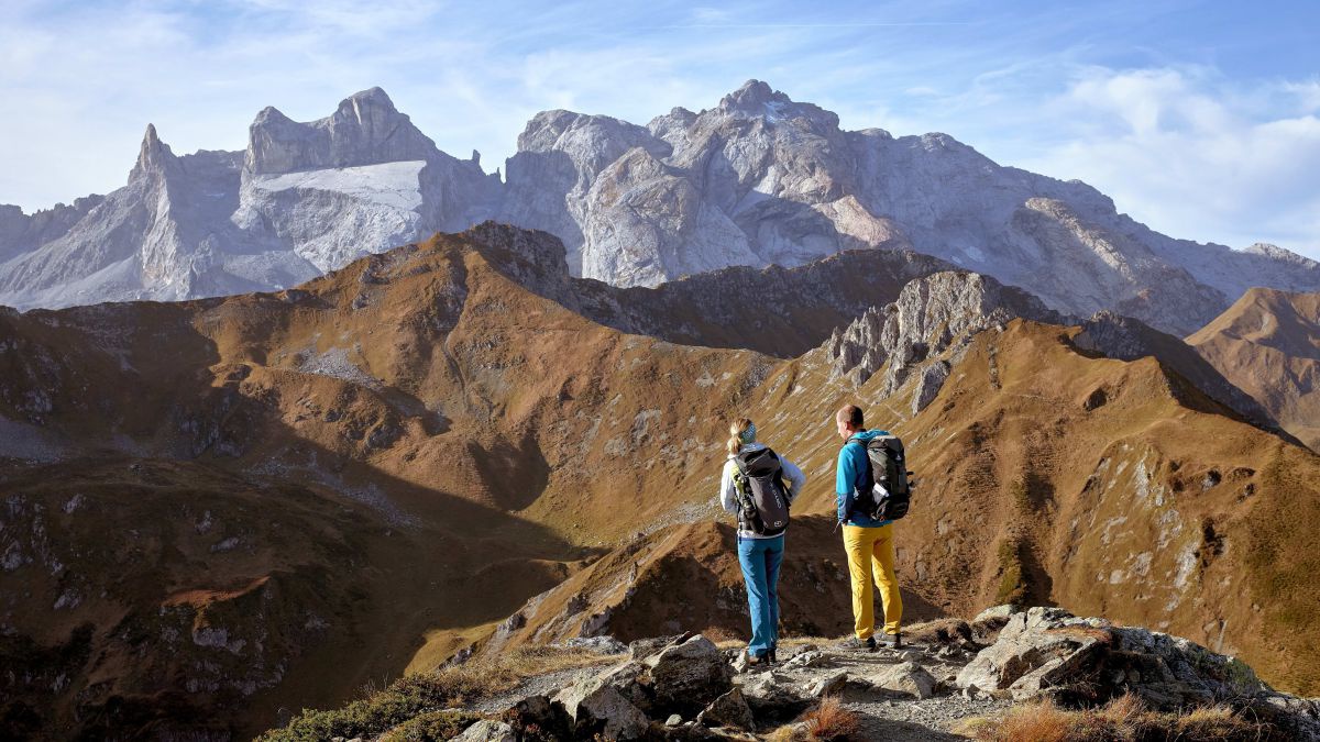 Mann und Frau wandern in hochalpiner Landschaft und genießen das Panorama.